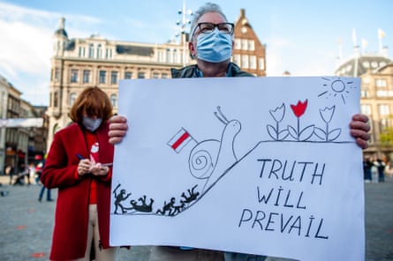 A man in a facemask holds a poster saying ‘truth will prevail’ in a public city square