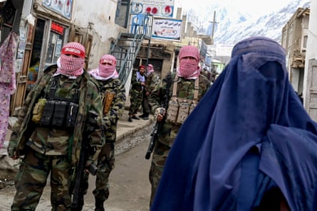 Armed men in military fatigues stand in a town street as a burqa-clad woman walks past