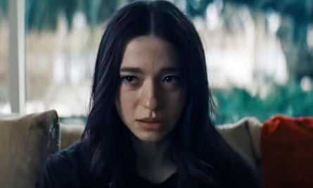 A woman with dark long hair looks somber sitting on a couch