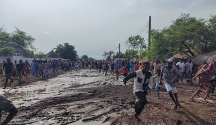 A crowd of people running down either side of a muddy street