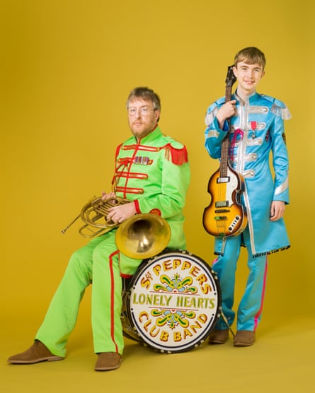 John Harris sitting on a Sgt Peppers drum holding a brass instrument with James standing by his side holding a guitar