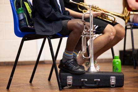 The legs of two seated students holding their trumpets in a practice room