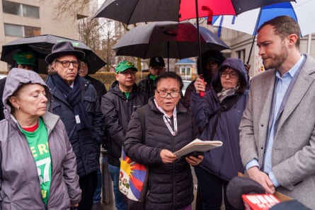 A middle-aged woman carrying a bag with a Tibetan flag reads out a statement surrounded by nine solemn-looking people