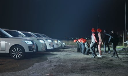 A night-time shot of gunmen forced a row of men in orange hoods to kneel in front of a row of cars with their headlights on