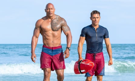 In wet lifeguard shorts looking insanely ripped, they walk down the beach