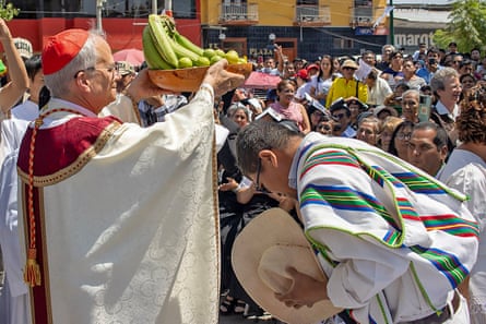 A clergyman receives a plate of fruit as a crowd stands by outside