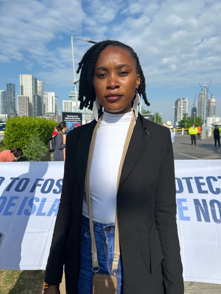 A woman stands in front of a banner with the London financial district skyline behind her.