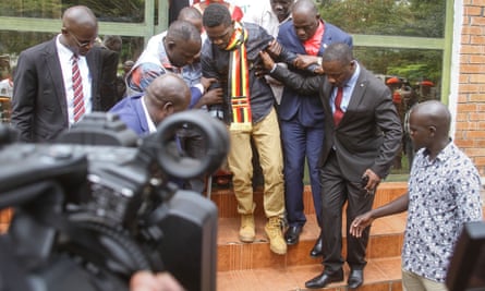 People hold on to Bobi Wine (centre) to help him walk down steps outside the court